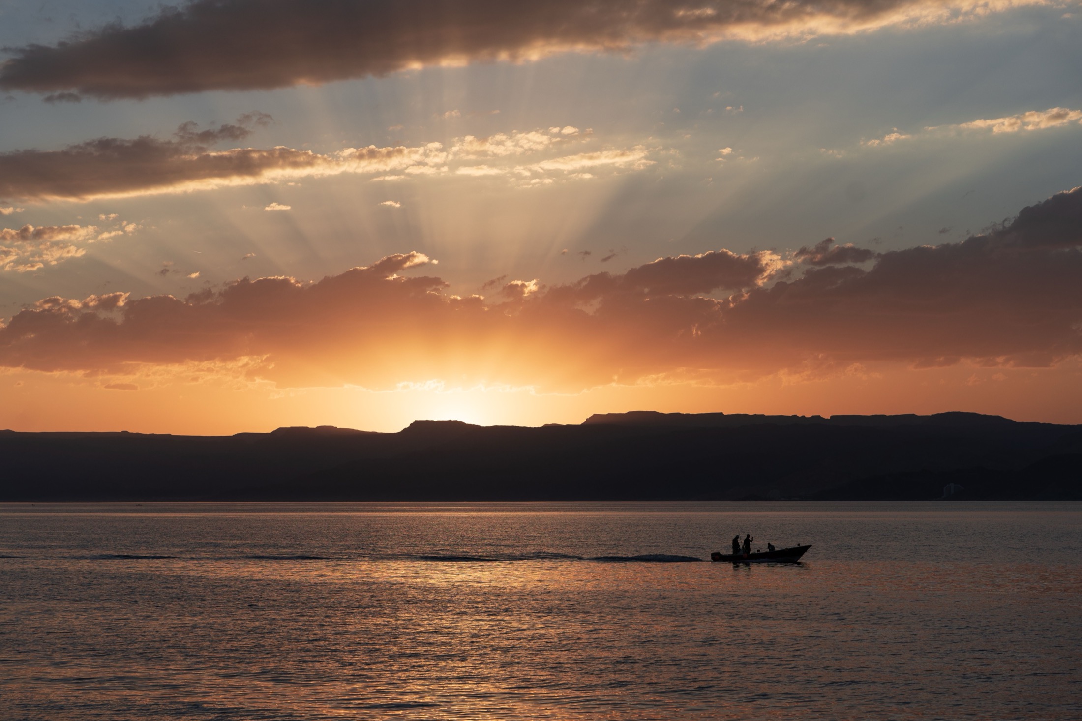 Two anglers running a bass boat across open water at sunrise